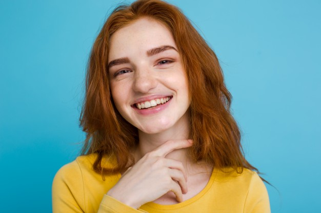 headshot-portrait-of-happy-ginger-red-hair-girl-with-freckles-smiling-looking-at-camera-pastel-blue-background-copy-space_1258-789